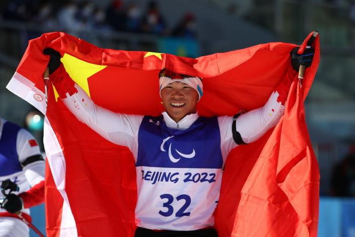A male Para athlete smiles while raising the Chinese flag above his head